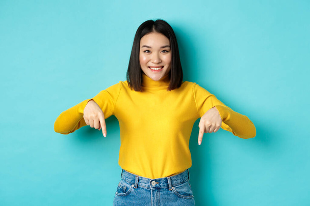 Koncepcja zakupów. Piękna koreańska dziewczyna ze szczęśliwym uśmiechem, wytykająca palcami sztandar, stojąca na niebieskim tle - Zdjęcie, obraz