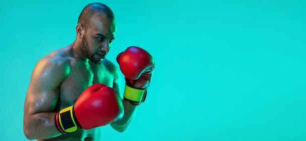 Szórólap. Egy profi bokszoló a piros kesztyű képzés, gyakorlása elszigetelt kék zöld háttér neon fény. - Fotó, kép