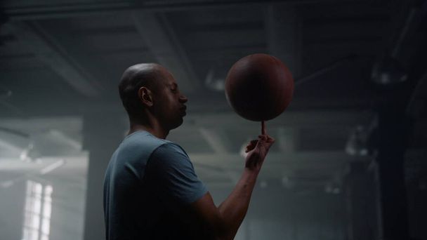 Retrato de jugador de baloncesto serio haciendo girar la pelota de baloncesto en el dedo en el gimnasio - Foto, Imagen