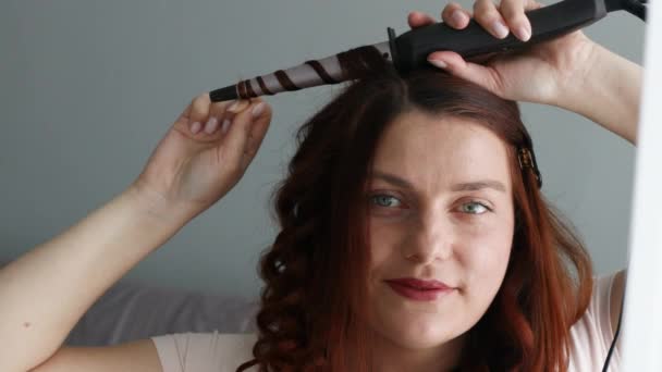 Belle fille aux longs cheveux roux faire sa coiffure avec sèche-cheveux en fer - Séquence, vidéo