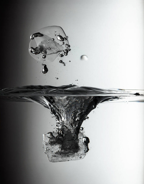 Ice piece drops into the water creating a splash. Selective focus. - Фото, зображення