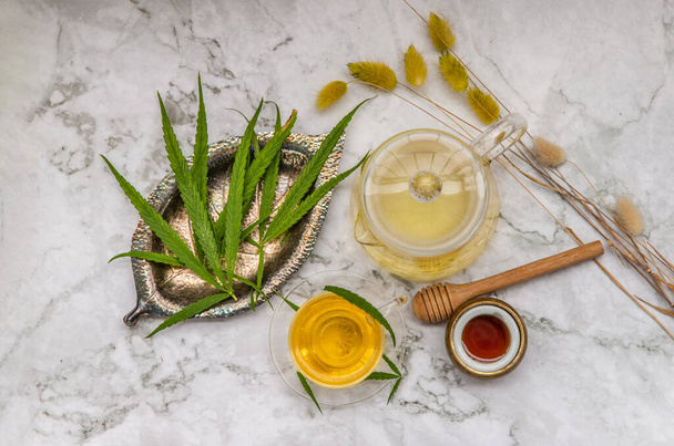 Refreshing and enjoy with A cup of Cannabis herbal tea and Stem with green marijuana leaves with honey on marble table for medical purposes for sleep and anxiety. Herbal tea and healthy drinks concept. Top view, Copy space, Selective focus. - Foto, Imagem