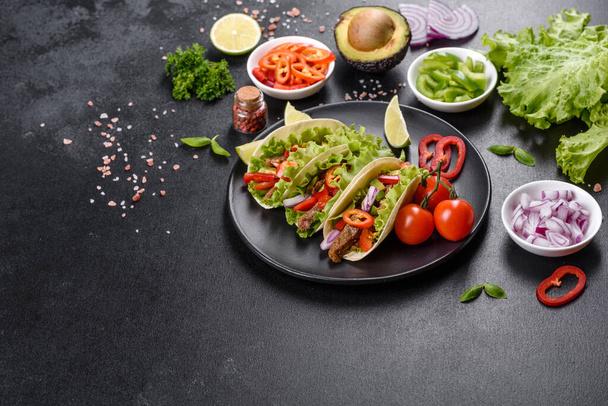Meksykańskie tacos z wołowiną, pomidorami, awokado, cebulą i sosem salsa na ciemnym, betonowym tle - Zdjęcie, obraz