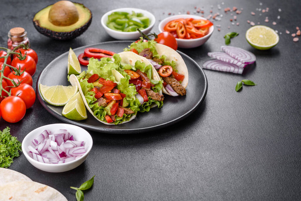 Mexican tacos with beef, tomatoes, avocado, onion and salsa sauce on a dark concrete background - Photo, Image