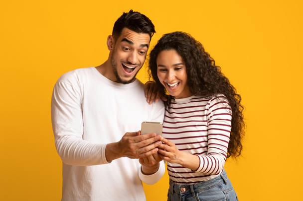 Cool App. Emocionada pareja árabe mirando la pantalla del teléfono inteligente en las manos - Foto, imagen