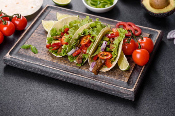Mexican tacos with beef, tomatoes, avocado, onion and salsa sauce on a dark concrete background - 写真・画像