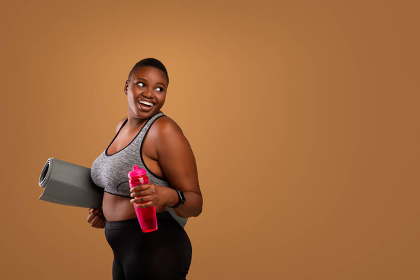 Jovem mulher negra posando com esteira e água no estúdio - Foto, Imagem