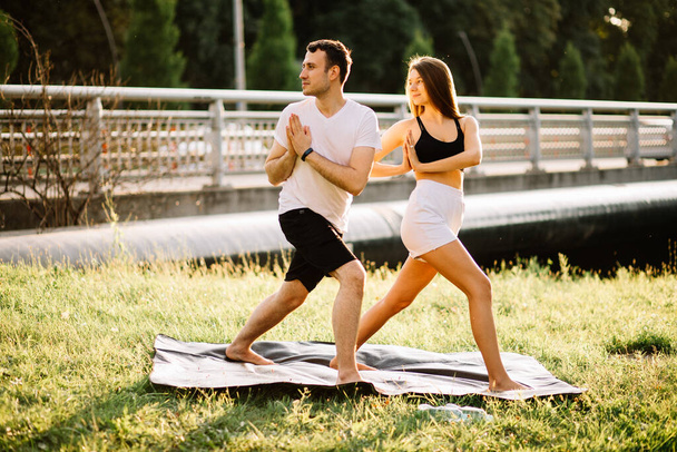 Young couple man and woman doing sports, yoga on city lawn, summer evening, stretching together on sunset, concentration on sunset - Foto, imagen