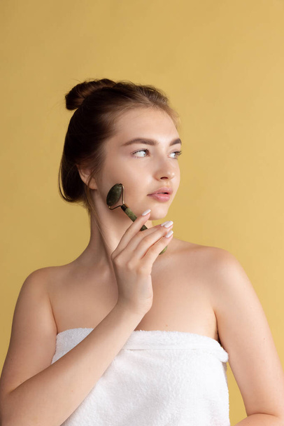 Close up portrait of young female fashion model isolated on yellow studio background. Beautiful caucasian woman making face massage. - Φωτογραφία, εικόνα