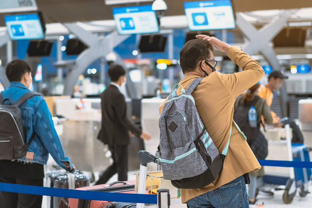 Rückansicht von Flugpassagieren, die eine Gesichtsmaske tragen, um Coronavirus (Covid-19) zu verhindern, warten am Check-in-Schalter im Flughafen, während das Personal eine Gesichtsmaske trägt. Neues normales Reisekonzept nach Covid-19-Pandemie. - Foto, Bild