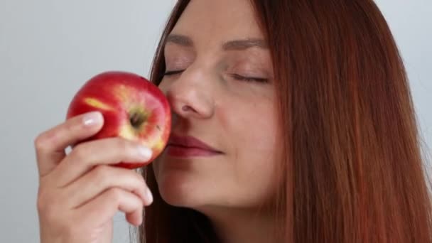 Happy young woman holding fresh ripe red apple in hand and smells organic fruit isolated on gray background. - Imágenes, Vídeo