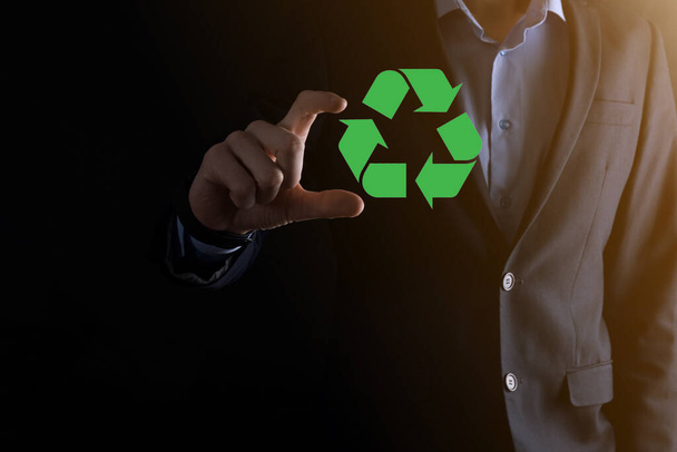 Un homme d'affaires en costume sur fond sombre tient une icône de recyclage, signe dans ses mains. Écologie, environnement et concept de conservation. Néon rouge lumière bleue. - Photo, image