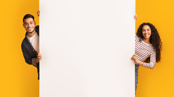 Fröhliches junges arabisches Paar steht neben großer weißer Werbetafel - Foto, Bild
