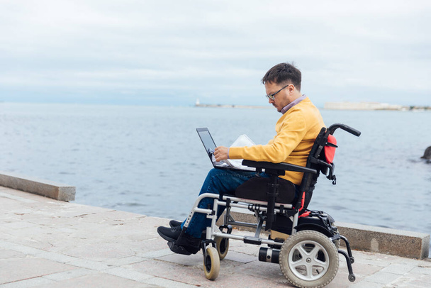 un hombre con discapacidad en una silla de ruedas trabaja en un ordenador en Internet - Foto, Imagen