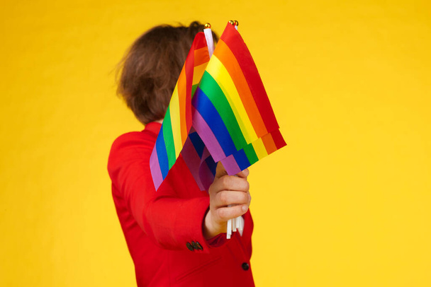 Jovem mulher irreconhecível segurando pequena bandeira LGBT em fundo de cor brilhante - Foto, Imagem