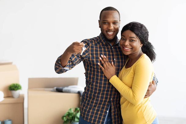 Szczęśliwi afrykańscy małżonkowie demonstrujący klucze do domu przed kamerą i obejmujący - Zdjęcie, obraz