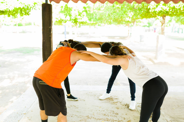 Wir schaffen das! Aktive Gruppe von Freunden umarmt und plaudert im Park, bevor sie mit ihrem Workout beginnen  - Foto, Bild