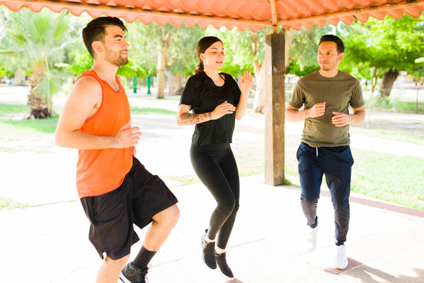 Νιώθω ιδρωμένος. Δύο Λατίνοι άνδρες και μια νεαρή γυναίκα τρέχουν στη θέση τους και την άσκηση με ένα καρδιο προπόνηση σε εξωτερικούς χώρους - Φωτογραφία, εικόνα