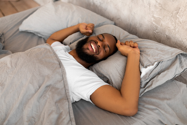 Tevreden jonge Afro-Amerikaanse man stretching na wakker worden - Foto, afbeelding