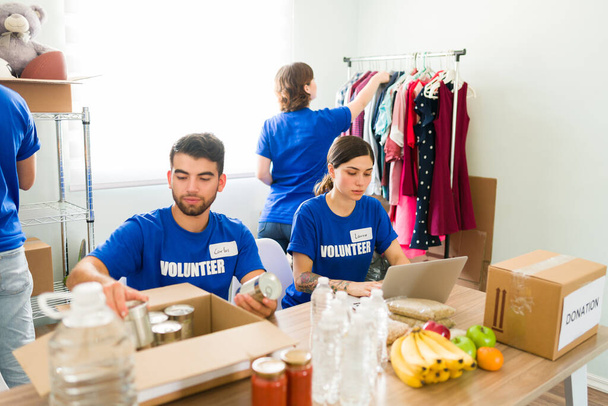 Группа латиноамериканских молодых волонтеров, работающих над организацией пожертвований продуктов питания и одежды в центре донорства - Фото, изображение