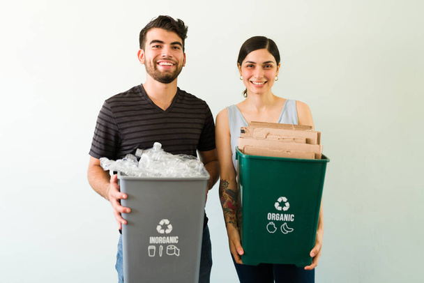 Good-looking responsible couple ready to put plastic and cardboard on the recycling bin against a white background - Photo, Image