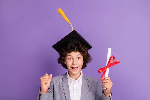 Photo of excited crazy winner schoolboy hold diploma enjoy triumph wear hat grey suit isolated violet color background - Фото, изображение