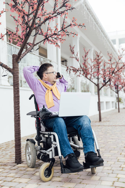 ένας άνδρας με αναπηρίες σε αναπηρικό καροτσάκι που μιλάει σε ένα smartphone - Φωτογραφία, εικόνα
