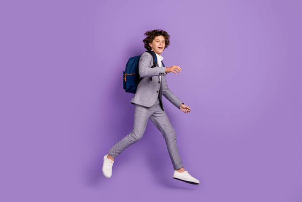 Photo of nice funky active pupil guy jump run move wear backpack grey suit footwear isolated violet color background - Fotó, kép