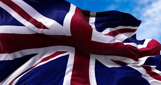De nationale vlag van het Verenigd Koninkrijk wappert in de wind. Buiten en lucht op de achtergrond. - Foto, afbeelding