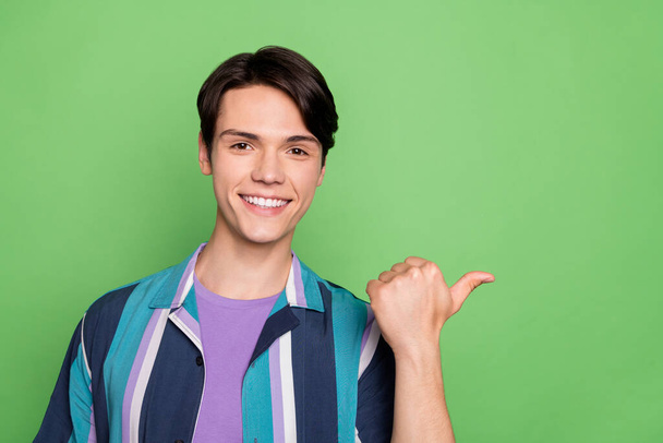 Photo of cute brunet millennial guy point space wear blue shirt isolated on green color background - Photo, Image