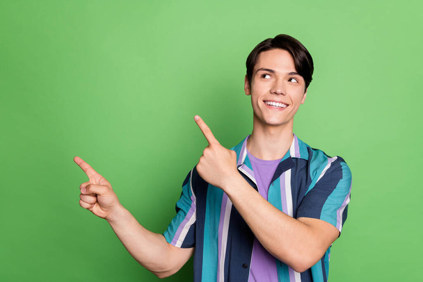 Photo of cheerful young happy positive man look point finger empty space smile isolated on green color background - Photo, Image