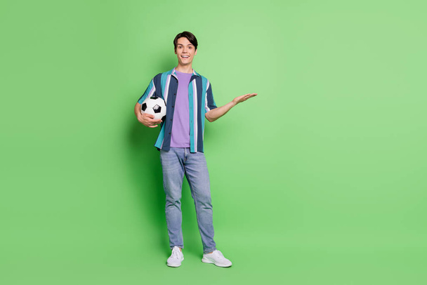 Full size photo of young happy cheerful man wear jeans hold hand empty space isolated on green color background - Foto, Imagen