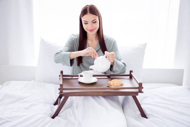 Photo of adorable sweet young woman gray nightwear smiling lying bed pouring tea indoors house home room - Fotografie, Obrázek