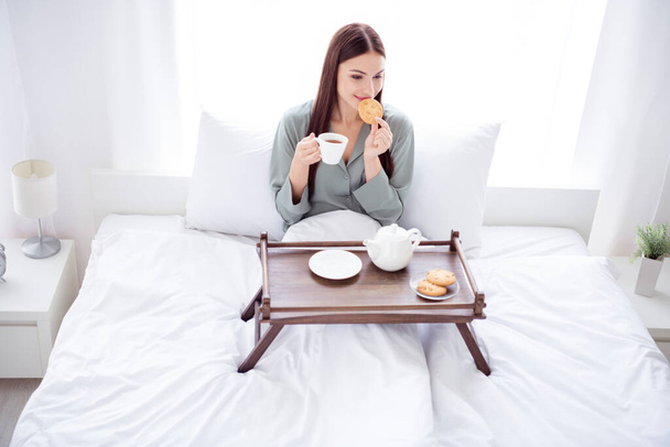 Full length body size photo woman sitting on bed in the morning drinking coffee with cookies - Foto, Imagem