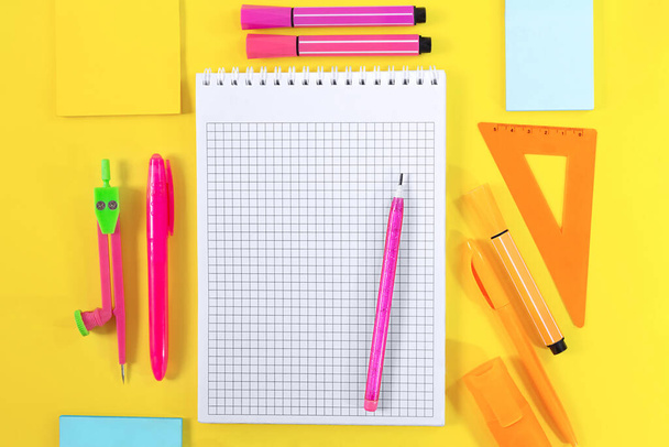 Back to school. Notebook checkered with pencil for notes for text. Nearby yellow, pink, orange stationery. Ruler, markers, felt tip pens, adhesive note, pens, compasses. Learning concept. Copy space - Photo, image