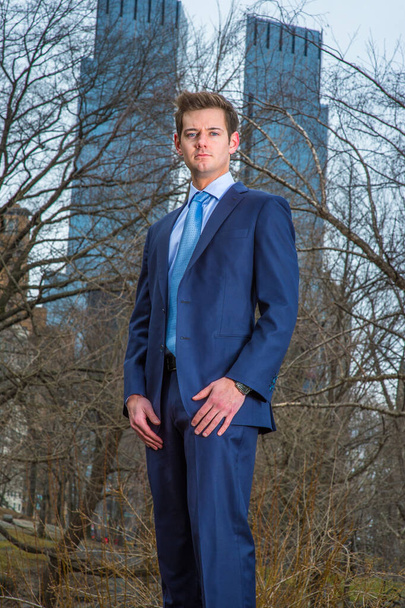 Dressing formally a young professional is standing outside and thoughtfully looking at you. The background is two high business buildings - Photo, Image