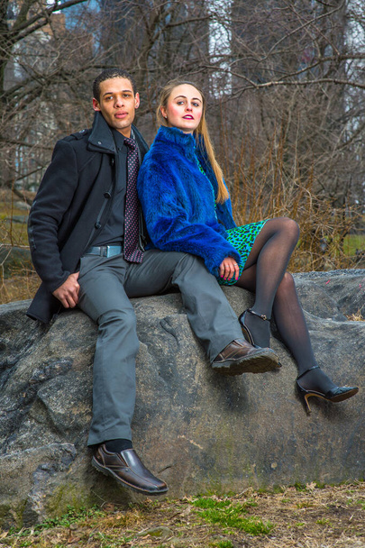 Um jovem casal está sentado em rochas no exterior no inverno, relaxando - Foto, Imagem