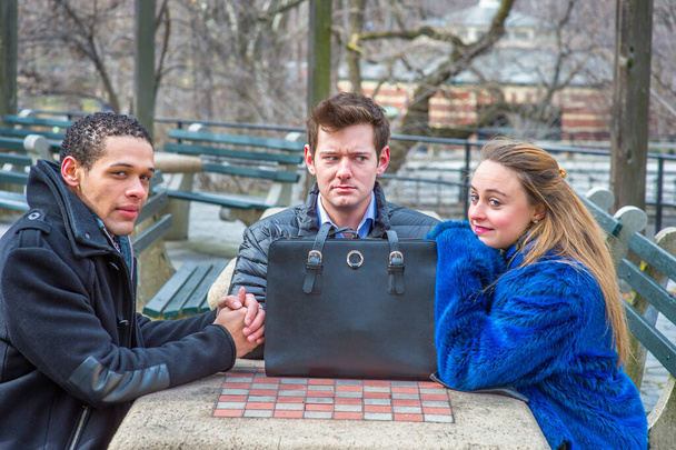 Three students are sitting by a table in a chilling winter, waiting for you. One guy looks mad - Foto, imagen