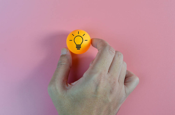 Ruka drží oranžovou kouli se symboly žárovky - Fotografie, Obrázek