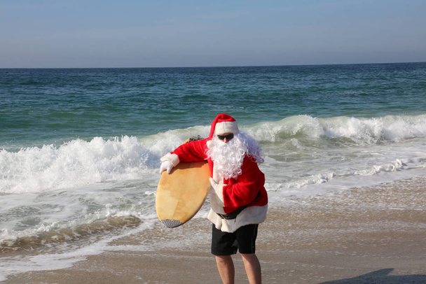 Vánoce. Santa Claus. Surfování. Santa Claus Surfování. Surfující Santa. Surfující Santa. Santa Claus Surfuje na své surfovací prkno, zatímco na krásné pláži s modrým oceánem. Soustřeď se na Santa Clausovu dovolenou. Santa chodí surfovat. Santa Claus na pláži. - Fotografie, Obrázek
