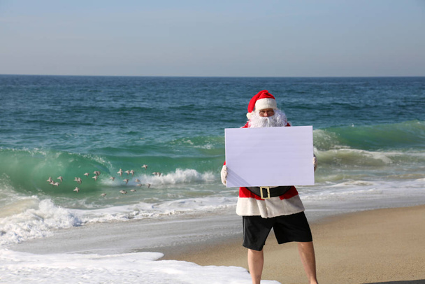 Noel zamanı. Noel Baba. Plajda boş beyaz tabelası olan Noel Baba. Mesaj için yer var. Noel Baba 'nın elinde boş bir beyaz tabela var. Noel Baba boş bir işaretle izole edildi. Mesajın ya da resmin için yer aç. Mutlu noeller. İyi tatiller. Mevsimler Selamlar. Ho Ho Ho - Fotoğraf, Görsel