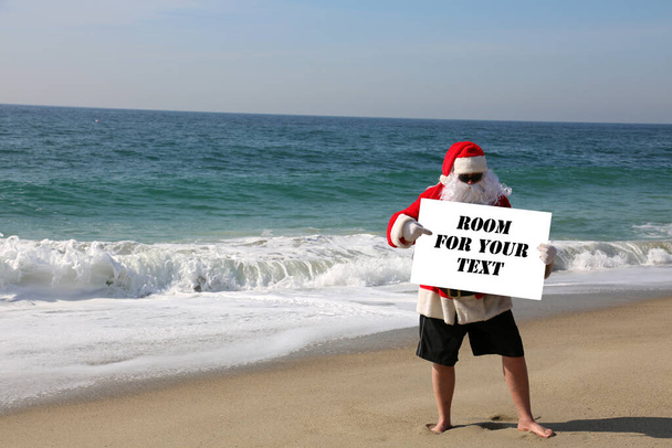 Święta. Święty Mikołaj. Święty Mikołaj na plaży z białym znakiem. Miejsce na smsa. Święty Mikołaj trzyma biały znak. Mikołaj odizolowany pustym znakiem. Miejsce na tekst lub obraz. Wesołych Świąt. Wesołych Świąt. Pozdrowienia. Ho Ho Ho - Zdjęcie, obraz