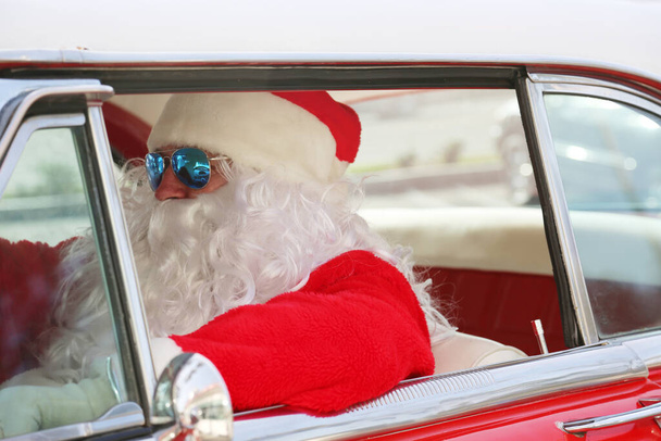 クリスマスだ。サンタクロース。サンタクロースの運転。ホットロッドカー。サンタクロースはホットロッドカーを運転する。サンタは車を運転する。サンタクロースがスタイルで到着します。クラシックカーのサンタクルーズ。サンタクロースが運転する。休暇でサンタクロース。サンタクロースロードトリップ. - 写真・画像