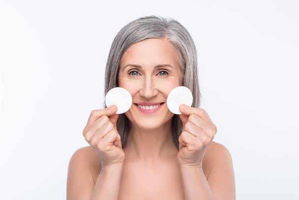 Photo of positive nice old woman hold cotton pads smile good mood skin care isolated on grey color background - Fotografie, Obrázek