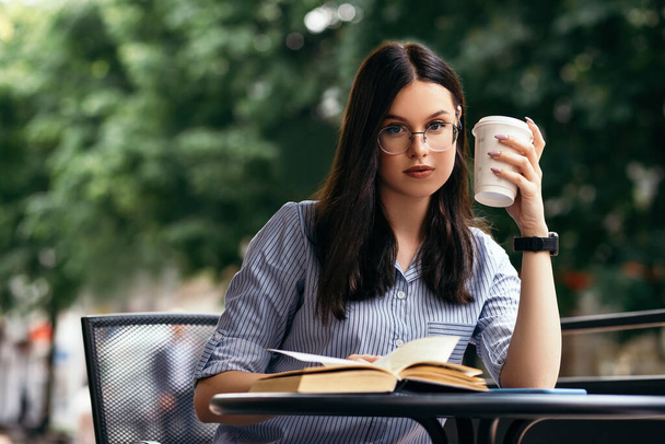 Business woman sitting outside terrace porch cafe drink hot beverage coffee break have lunch reading book smart watch hand wear stylish glasses copyspace. Rush hour, International Coffee Day  - Foto, imagen