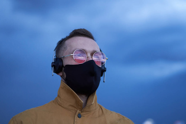 Человек в розовых очках, наушниках и черной маске для лица - Фото, изображение