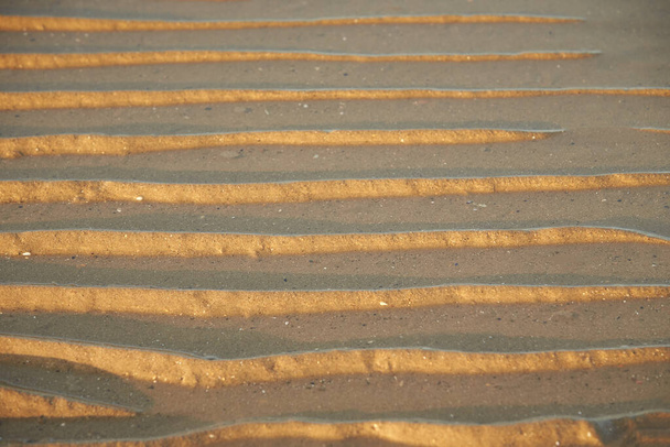 Піщані хвилі текстури з водою на морському пляжі. Жовта текстура піску для тла
. - Фото, зображення