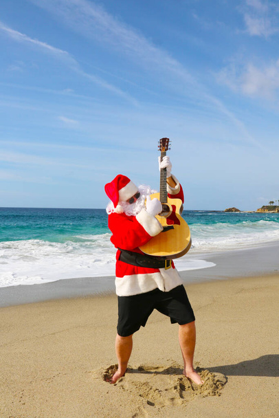 Рождество. Санта Клаус. Гитара. Санта. Санта Клаус играет на гитаре на пляже. Музыкальный Санта Клаус. Красивый бородатый солист Санта Клауса, играющий на гитаре. Санта веселится, играя на гитаре, чтобы все услышали. Счастливого Рождества. Рождественские песни. улыбка - Фото, изображение