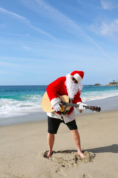 Рождество. Санта Клаус. Гитара. Санта. Санта Клаус играет на гитаре на пляже. Музыкальный Санта Клаус. Красивый бородатый солист Санта Клауса, играющий на гитаре. Санта веселится, играя на гитаре, чтобы все услышали. Счастливого Рождества. Рождественские песни. улыбка - Фото, изображение