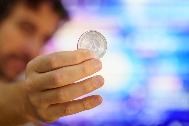 Muži držící cardanovskou minci, známí jako ADA mince. Je to jedna z nejoblíbenějších kryptografických mincí do budoucna. na základě éterické kryptoměny. Logo Cardano - Fotografie, Obrázek